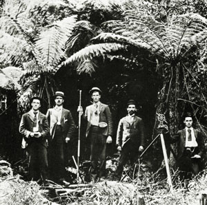 Black and white photo of five men and a camera on a tripod standing in a wooded area
