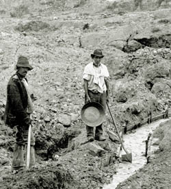 Two men standing next to a small ground sluice to pan for gold