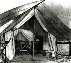 Black and white picture of a canvas tent with chests and a chair and table inside